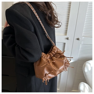 Detail of a brown pleated cloud bag with ribbon bows and a woven chain strap on a model