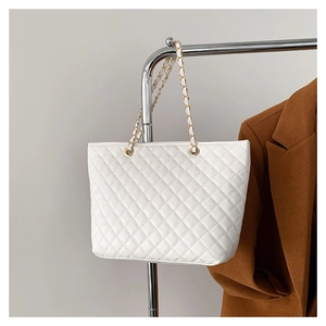 White quilted tote bag with gold chain strap hanging next to a stylish brown wool coat