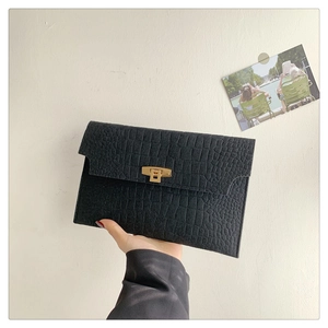 Close-up of black crocodile pattern envelope clutch with golden twist lock detail