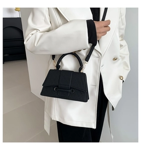 Detail of black textured square handbag with gold hardware styled on a white blazer
