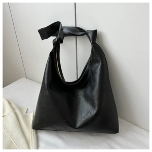 Minimalist black PU leather tote bag with unique knot shoulder strap detail in a studio setting