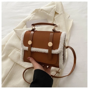 Detail of a brown and white PU leather handbag with faux shearling trim and gold buckles