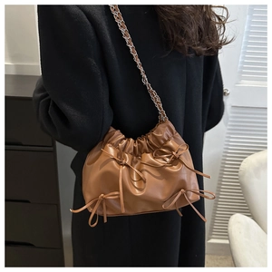 Detail of brown pleated bucket bag featuring elegant ribbon bows and silver chain strap