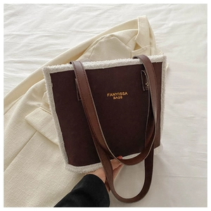 Detail of a brown suede tote bag with white faux shearling trim and golden logo text