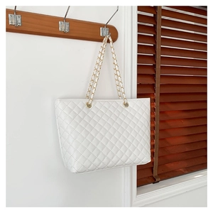 Elegante borsa tote trapuntata bianca con catena dorata appesa a una parete bianca