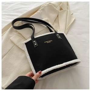 Close-up of black shoulder bag featuring white faux shearling trim and golden lettering