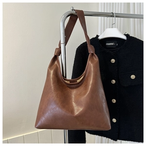 Close-up of brown PU leather hobo bag with knot detail hanging on a metal rack