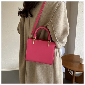 Detail view of a magenta square shoulder bag with gold hardware worn by a model