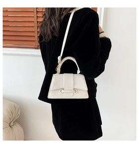 Detail view of white textured leather handbag with gold hardware and top handle