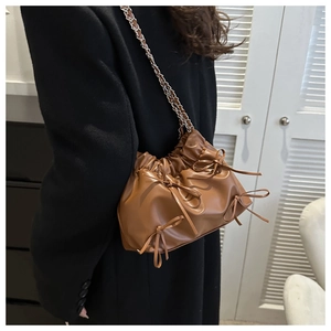 Close-up of brown pleated shoulder bag with bow details and silver chain strap
