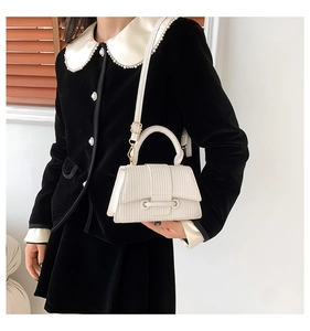 Close-up of a white textured leather crossbody bag with top handle and metal hardware detail