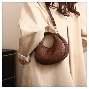Detail of woven texture on brown crescent shoulder bag with golden hardware
