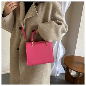 Detail of rose pink leather handbag with gold hardware styled on a beige wool coat