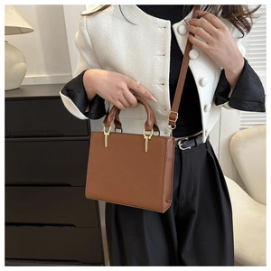 Close-up of minimalist brown square handbag featuring gold T-accents and chic stitching