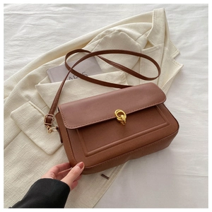 Détail d'un sac bandoulière marron avec fermoir tournant doré posé sur un blazer chic