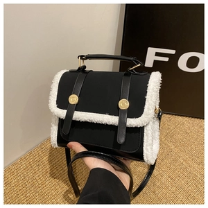 Detail of black leather handbag with white plush trim and golden hardware accents