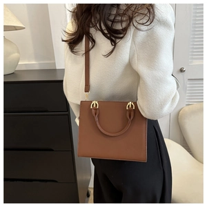 Brown rectangular crossbody bag with top handle and golden hardware on a female model