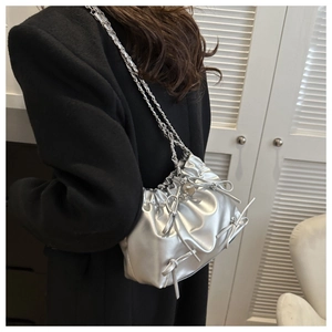 Close-up of silver pleated bucket bag with bow accents and chain strap on black coat