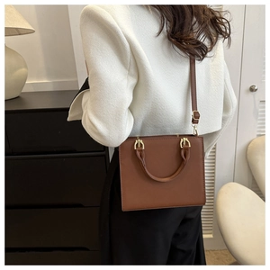 Detail view of brown leather handbag with gold hardware worn with a tweed jacket