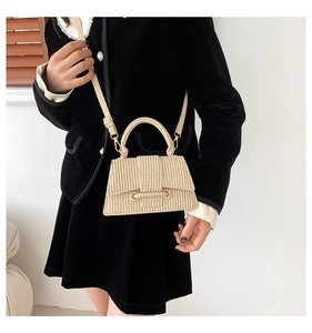 Detail of beige straw handbag with woven texture and gold hardware on a model