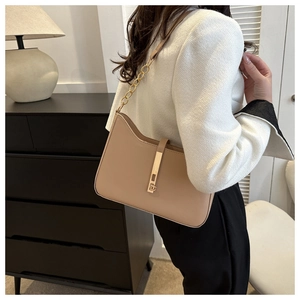 Detail shot of a minimalist beige shoulder bag with a gold vertical lock and chain strap
