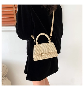 Rear view of a model wearing the beige woven trapezoid handbag with a metal strap hook