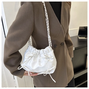 Detail of white pleated drawstring bag with ribbon bows and metal chain strap
