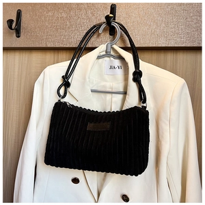 Close-up of black corduroy shoulder bag showing vertical texture and knotted strap details