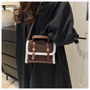 Detail of vintage brown leather and fleece crossbody bag styled on a black coat