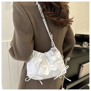 Close-up of white bucket bag featuring bow details and elegant metal chain strap
