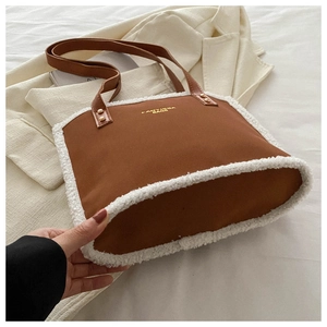 Detail of a brown suede tote bag featuring white faux fur trim and gold rivet accents