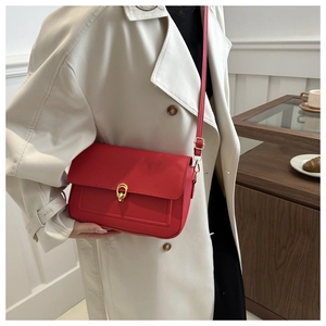 Détail d'un petit sac à bandoulière rouge vif avec un fermoir rotatif en métal doré