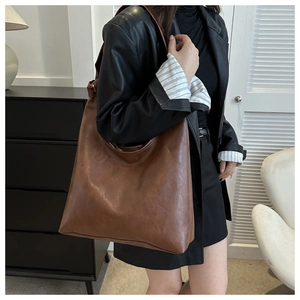 Side view of large vintage brown PU leather shoulder bag worn by model in a modern room
