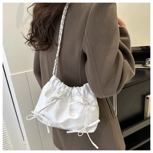 Detail view of white PU leather bucket bag with bow accents and chain shoulder strap