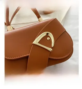 Detail view of brown faux leather saddle bag with signature gold D-shaped buckle