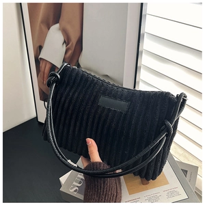 Detail of black corduroy shoulder bag with textured vertical stripes and leather patch