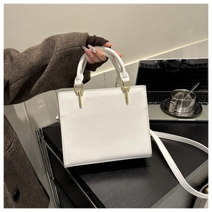 Minimalist white square handbag with top handle and gold hardware on office desk