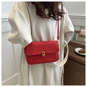 Sac bandoulière rouge en cuir PU avec boucle dorée porté sur un manteau crème