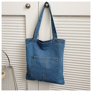 Detail of blue denim tote bag with dual front pockets on a white slatted background
