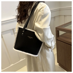 Detail of minimalist black shoulder bag with white faux fur trim and gold logo lettering