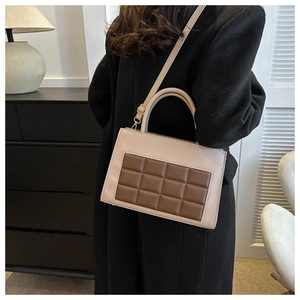 Detail of beige and brown crossbody bag with grid pattern on a dark cabinet