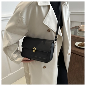 Détail du sac bandoulière en cuir noir avec boucle dorée et finition mate sur un mannequin