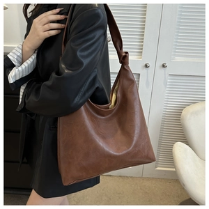 Detail of a brown PU leather tote bag with a knotted shoulder strap shown on a model