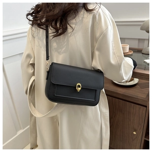 Détail du sac à bandoulière en cuir noir porté par un mannequin sur un manteau