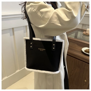 Close-up of black leather shoulder bag featuring white faux fur trim and gold lettering