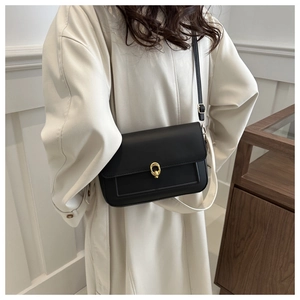 Détail d'un sac bandoulière en cuir noir avec fermoir doré porté par un mannequin