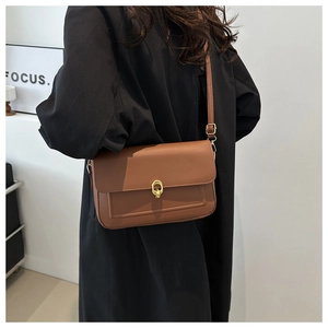 Détail d'un sac à bandoulière en cuir marron avec fermoir doré porté par un mannequin