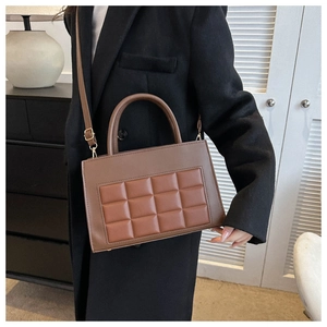 Detail of a brown quilted leather crossbody bag worn over a black wool coat