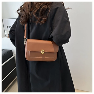 Détail d'un sac bandoulière marron caramel avec boucle dorée sur un blazer noir