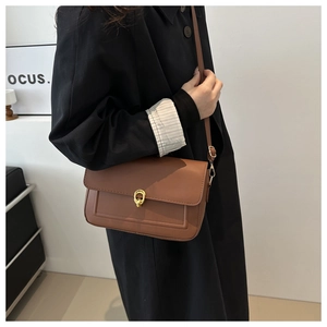 Détail d'un sac bandoulière marron en similicuir avec une boucle dorée sur le rabat